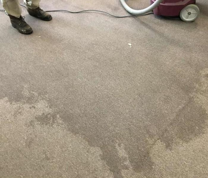 water stained carpet with machine and hose on right and someone standing on left with only boots showing