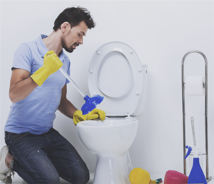 man at overflowing toilet with plunger figuring out what to do